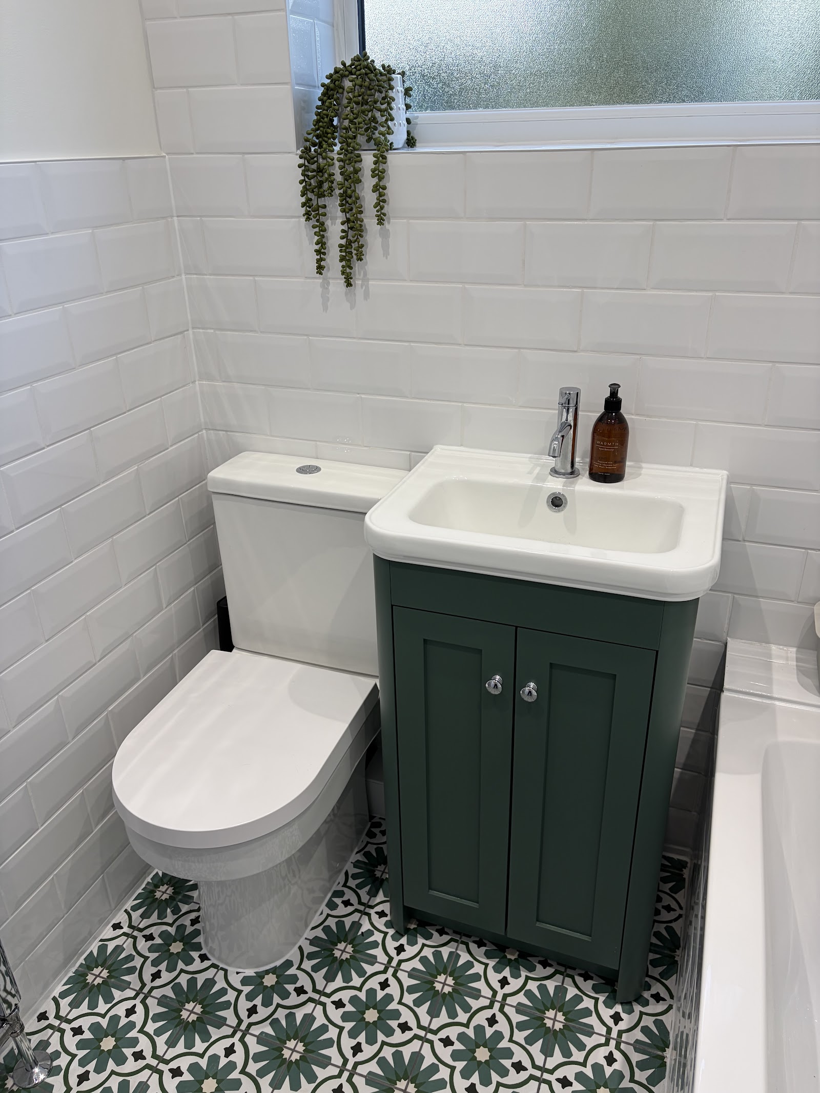 A compact cloakroom — combined toilet-and-basin unit in green, white metro tiling and patterned floor.