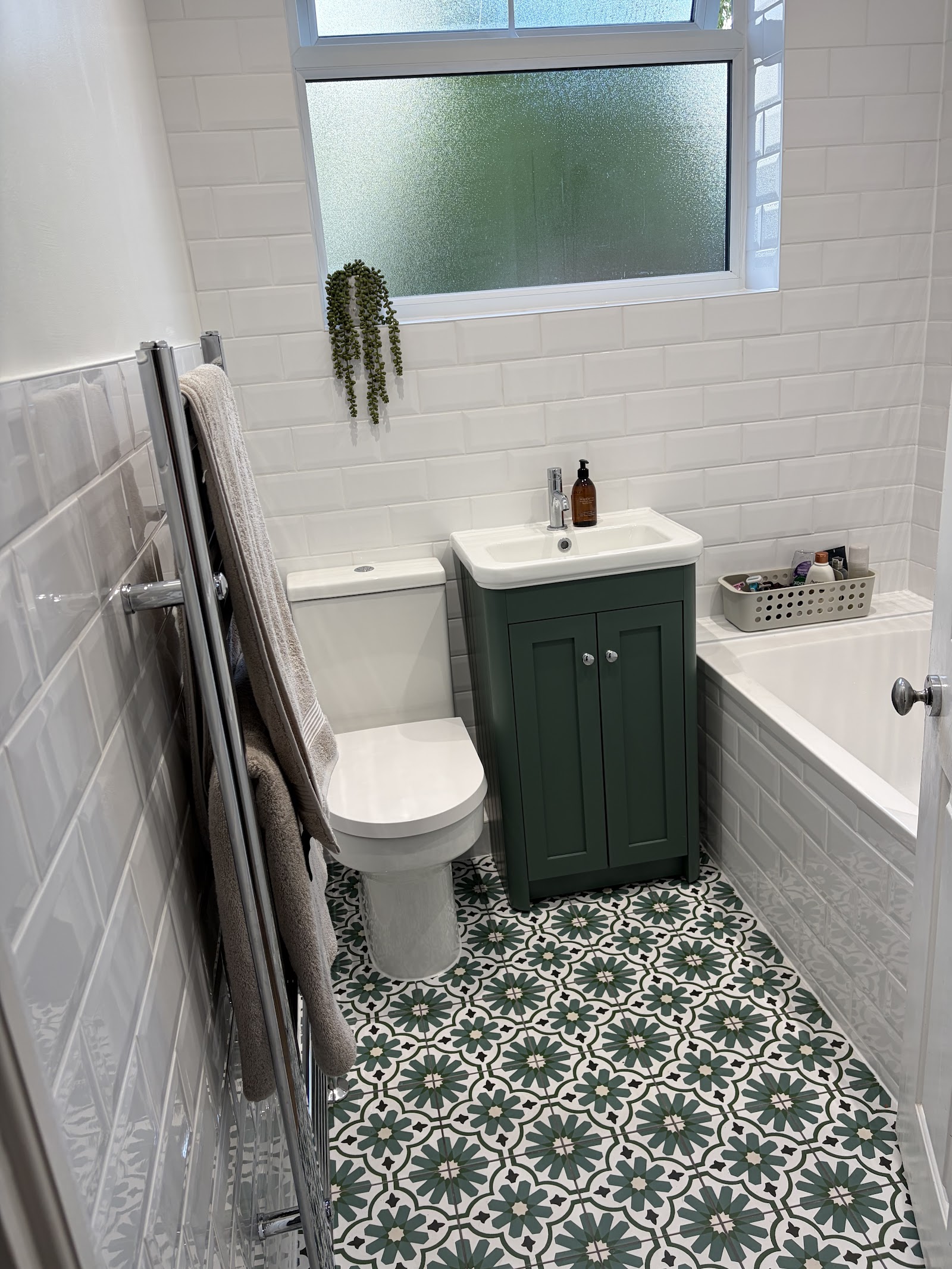 A bright family bathroom — white metro tiling, green vanity and patterned floor tiles over the bath.